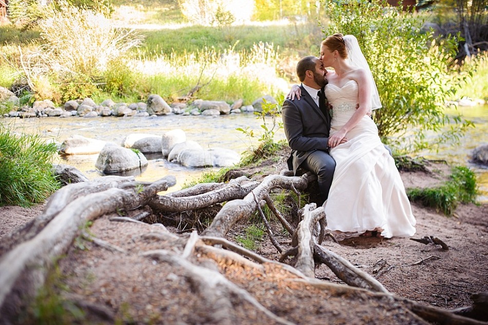 bride and groom sit next to river with cool tree roots